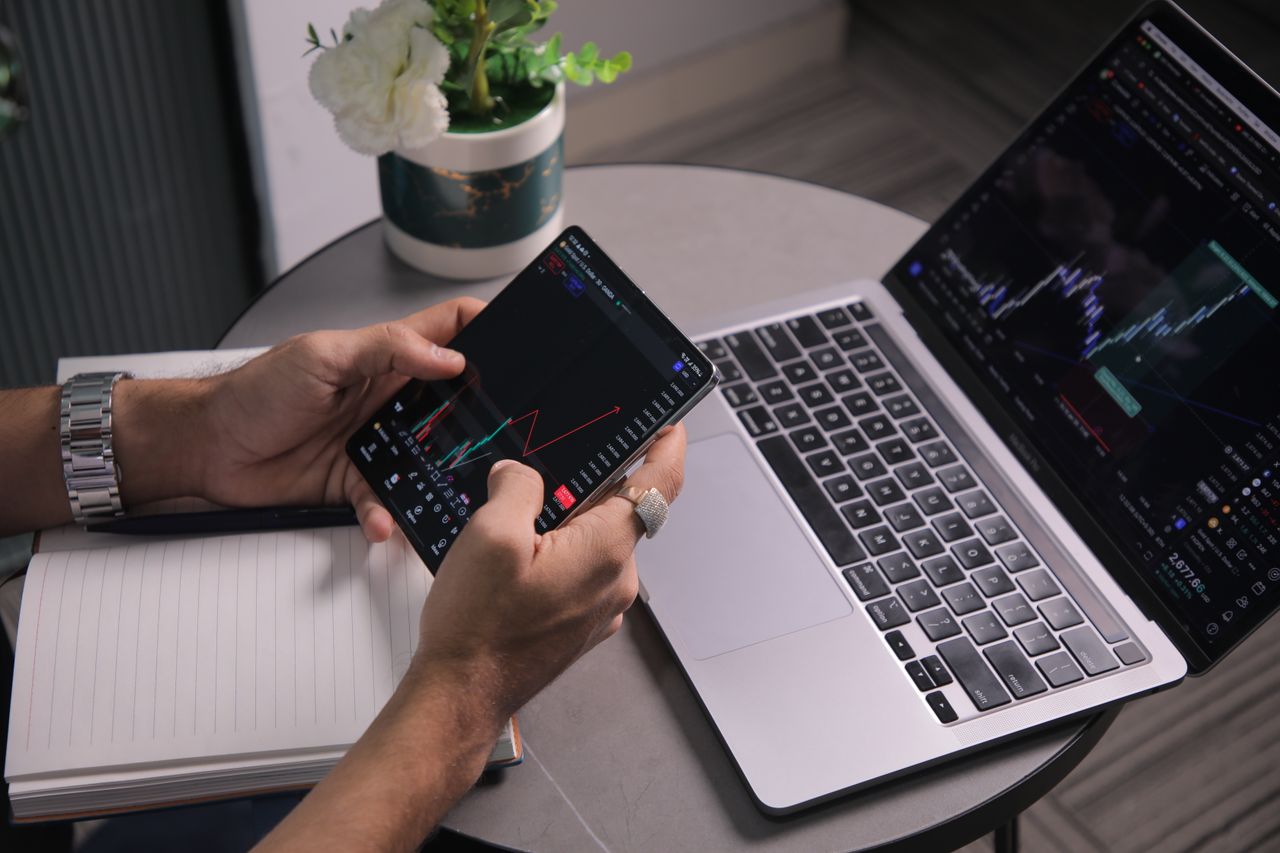 Services Man analyzing stock trends with laptop and mobile trading app at a modern workspace.