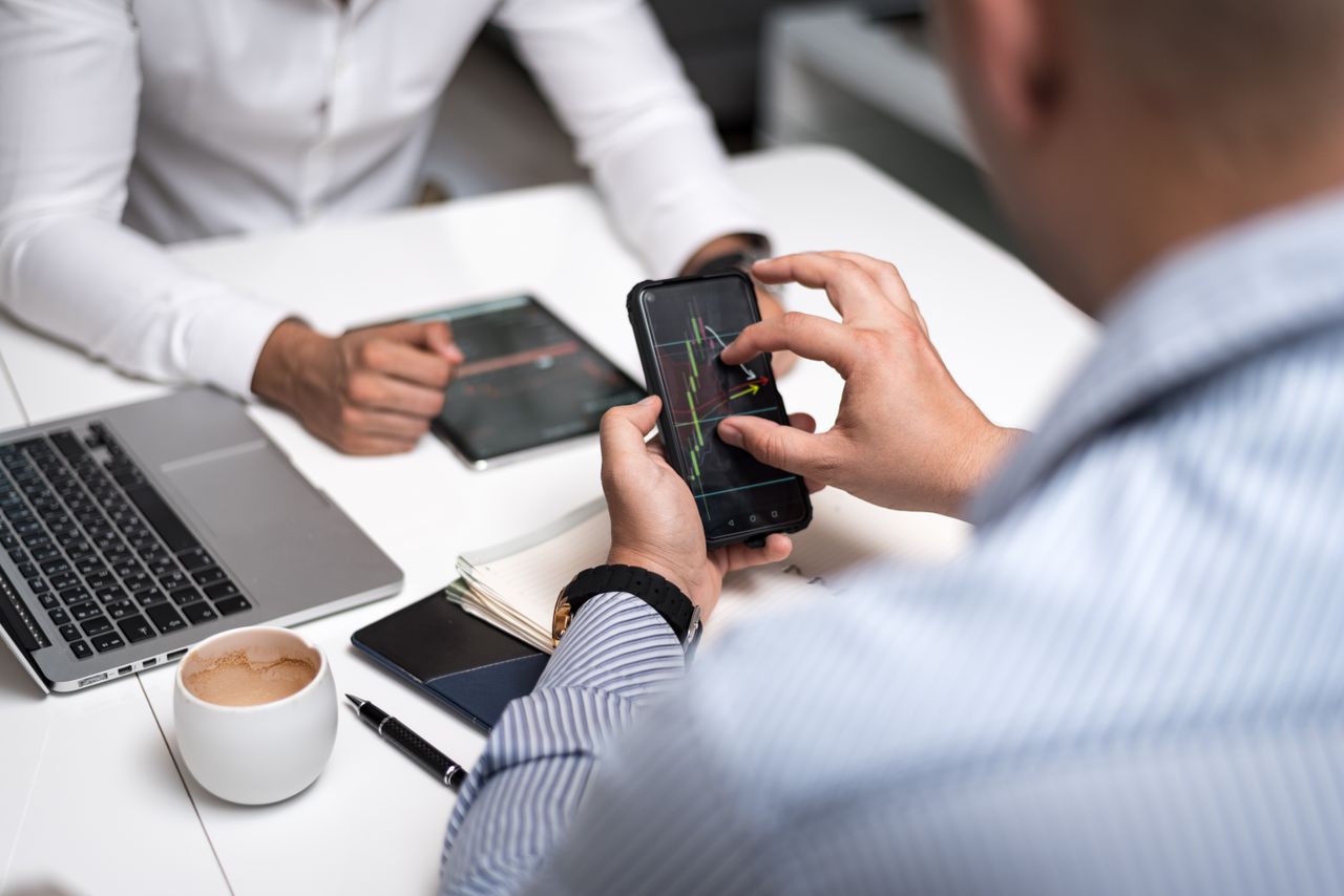 Services Business professionals using smartphones and tablets to analyze trading charts during a meeting.